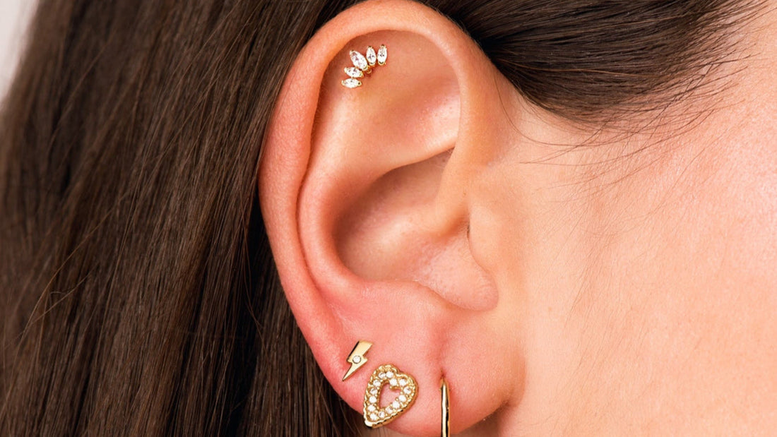 Oreille composée de plusieurs piercings en or : clou en hélix, clous et anneau aux lobes